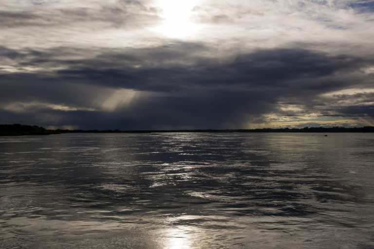 Fotografia colorida do mar e nuvens carregadas ao fundo, com o Sol saindo entre elas.